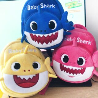 3 plush backpacks for children representing a cute shark. This one is placed on a flat table