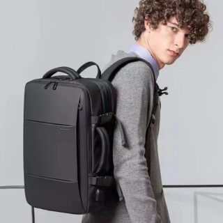 A young man carrying a black rectangular backpack on his shoulder. The bag has a zipper on the top and a handle on both sides.